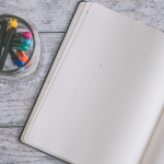 Blank notebook opened with a jar of colored pens on the table next to it.