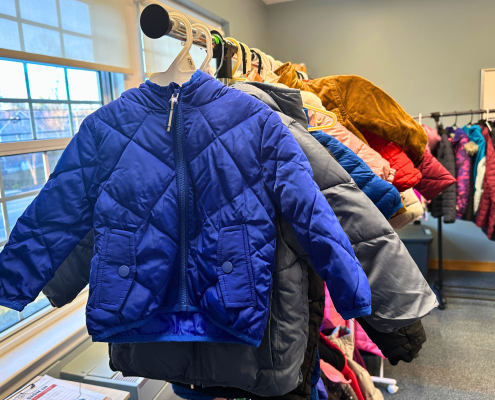 A row of various childrens winter jackets hanging on a clothing rack.