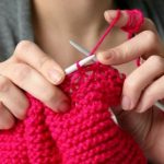 Hands shown knitting something pink