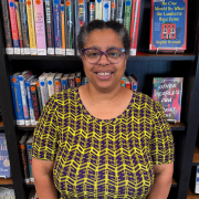 A woman wearing glasses smiling, wearing a black and yellow top.