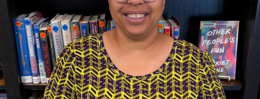 A woman wearing glasses smiling, wearing a black and yellow top.