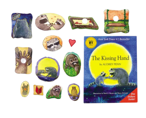 Assorted illustrated story stones depicting raccoons and scenes from “The Kissing Hand” are arranged next to a copy of the book with a blue and yellow cover.